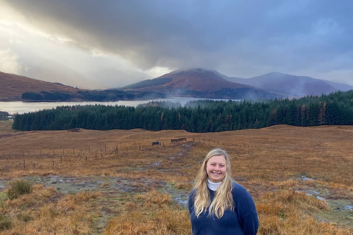 a person standing in a field with trees and mountains in the background