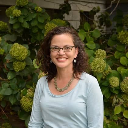 a person smiling in front of a bush