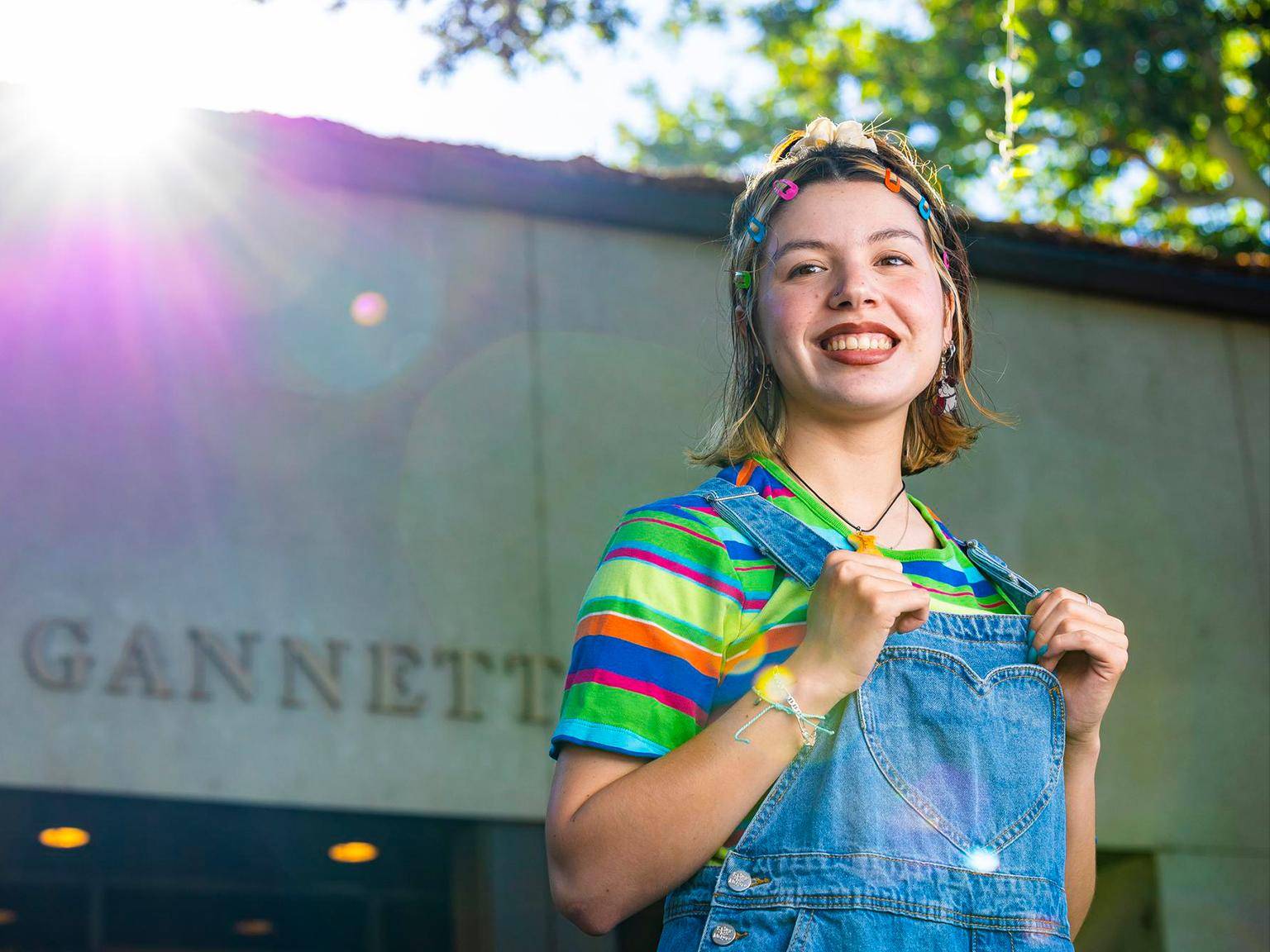 a person smiling with rainbow colored shirt and denim overalls