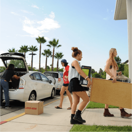 a group of people carrying boxes and moving into a parking lot