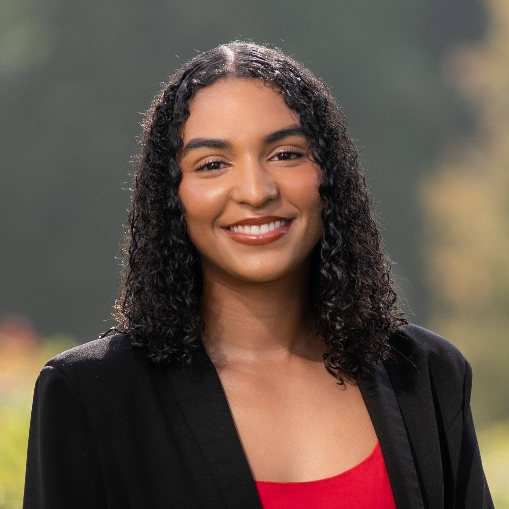 a person with curly black hair wearing a black jacket and red shirt