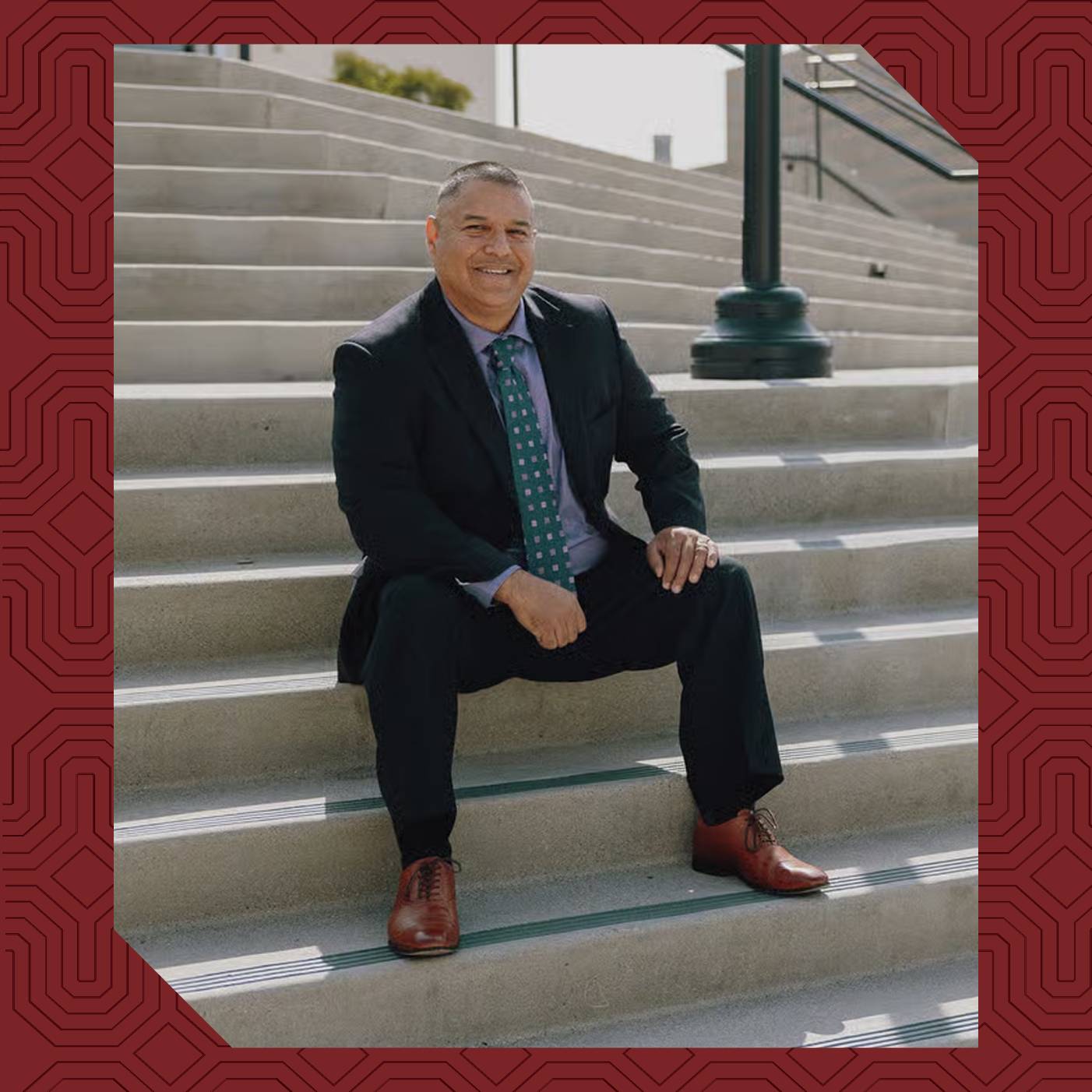 Fidel Chagolla ’23 sits on campus steps at University of Redlands wearing a suit and smiling.
