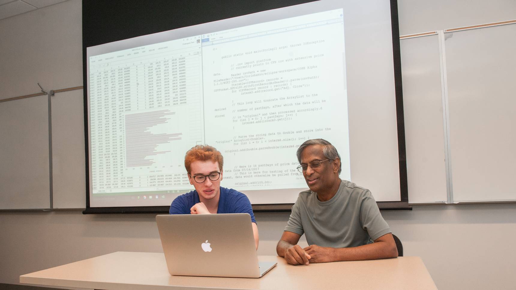 a person and person sitting at a table looking at a laptop