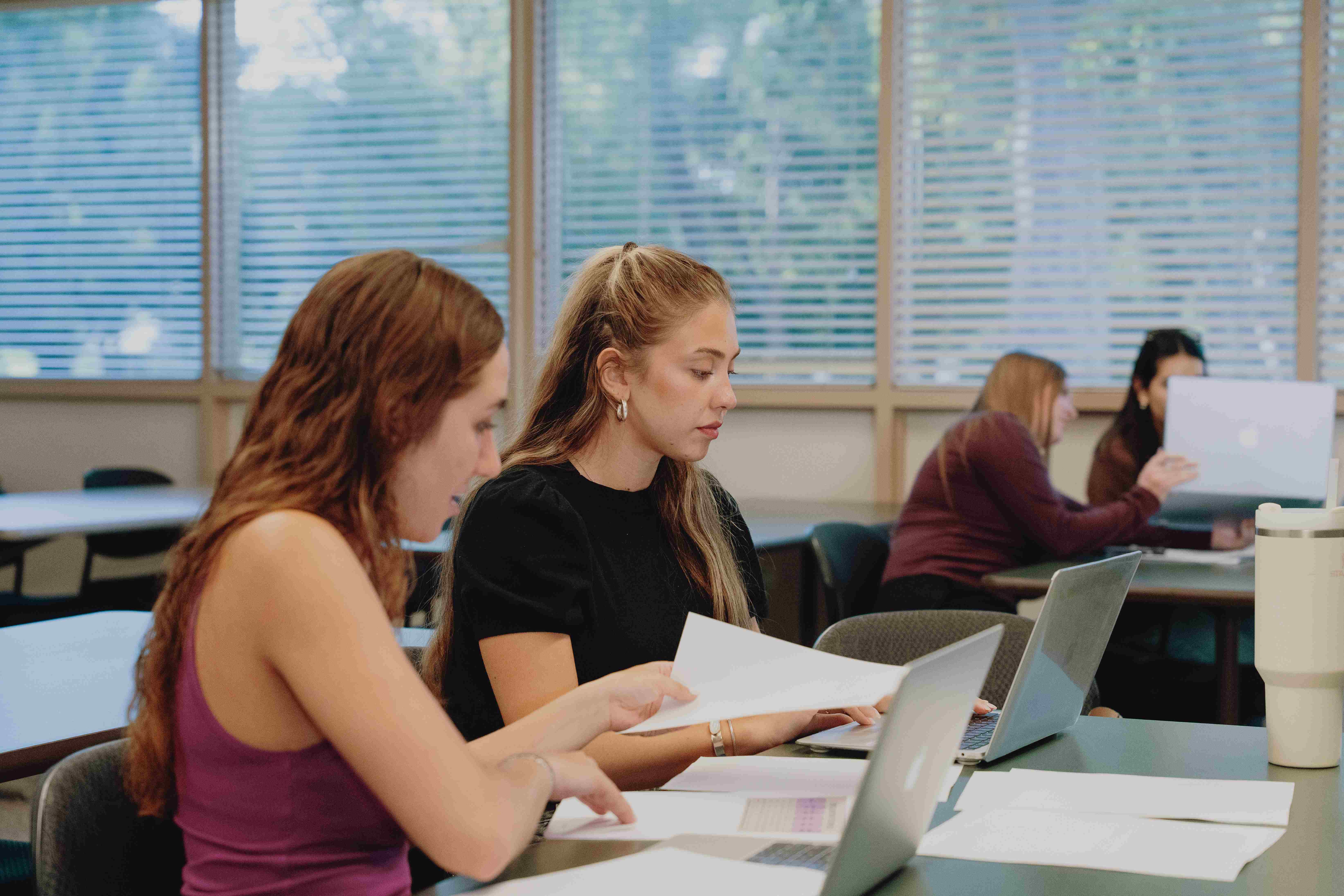 a group of women sitting at a table with laptops and papers