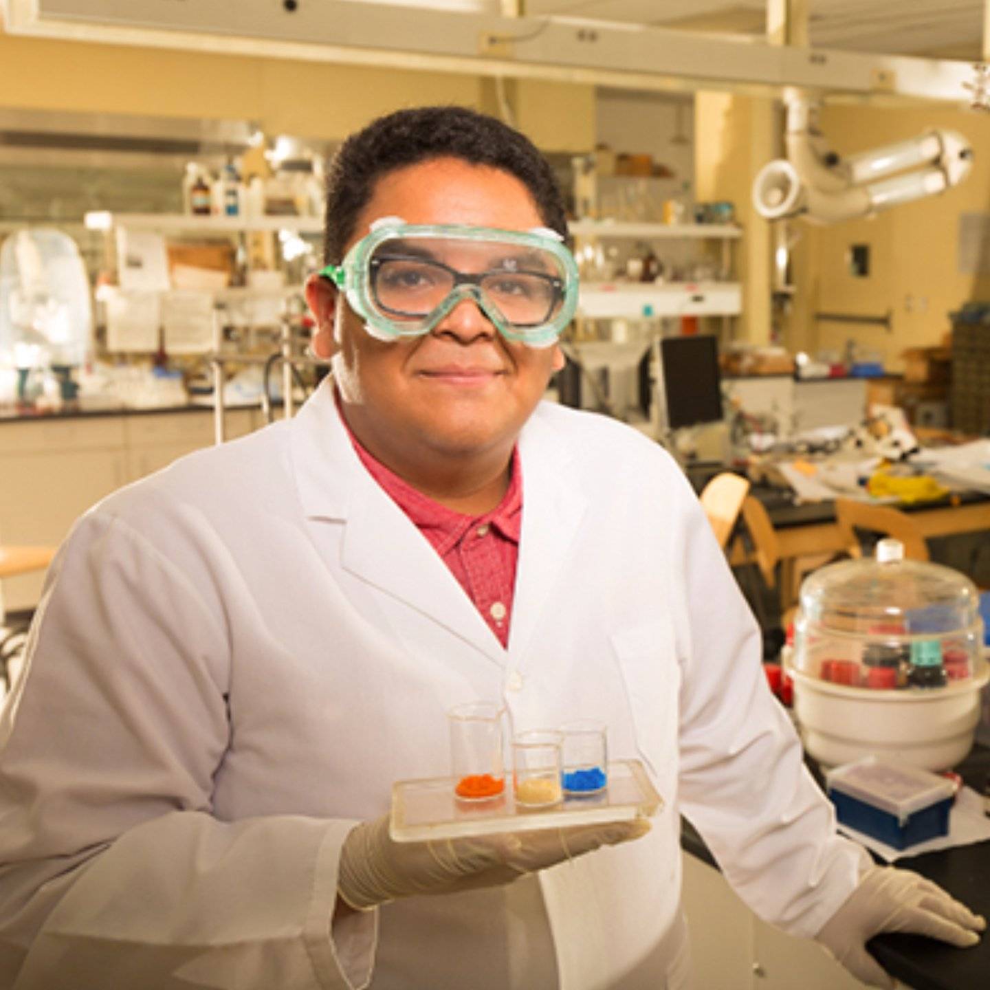 a person wearing a white coat and goggles holding a tray of test tubes