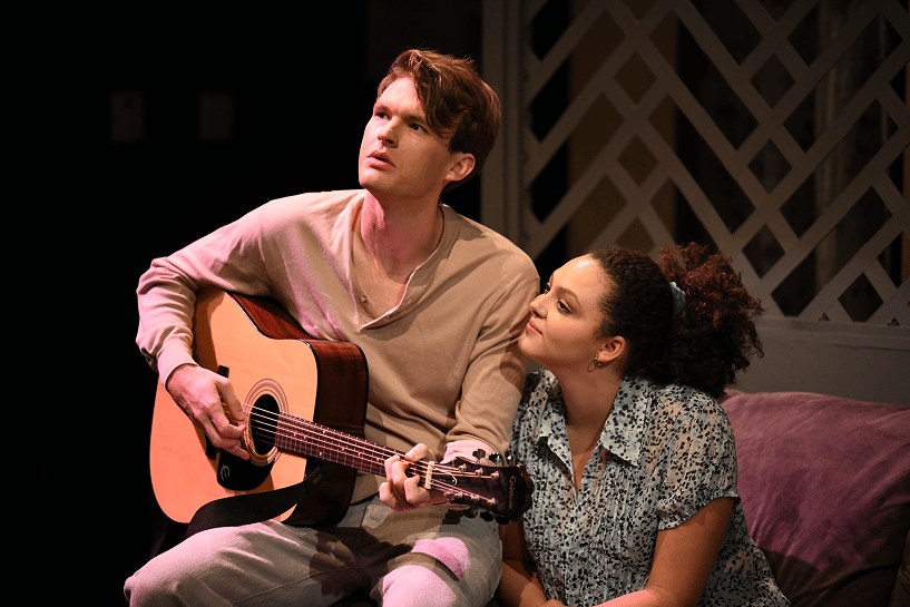 a person playing a guitar with a person sitting next to him