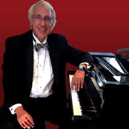 a person in a suit and bow tie playing a piano