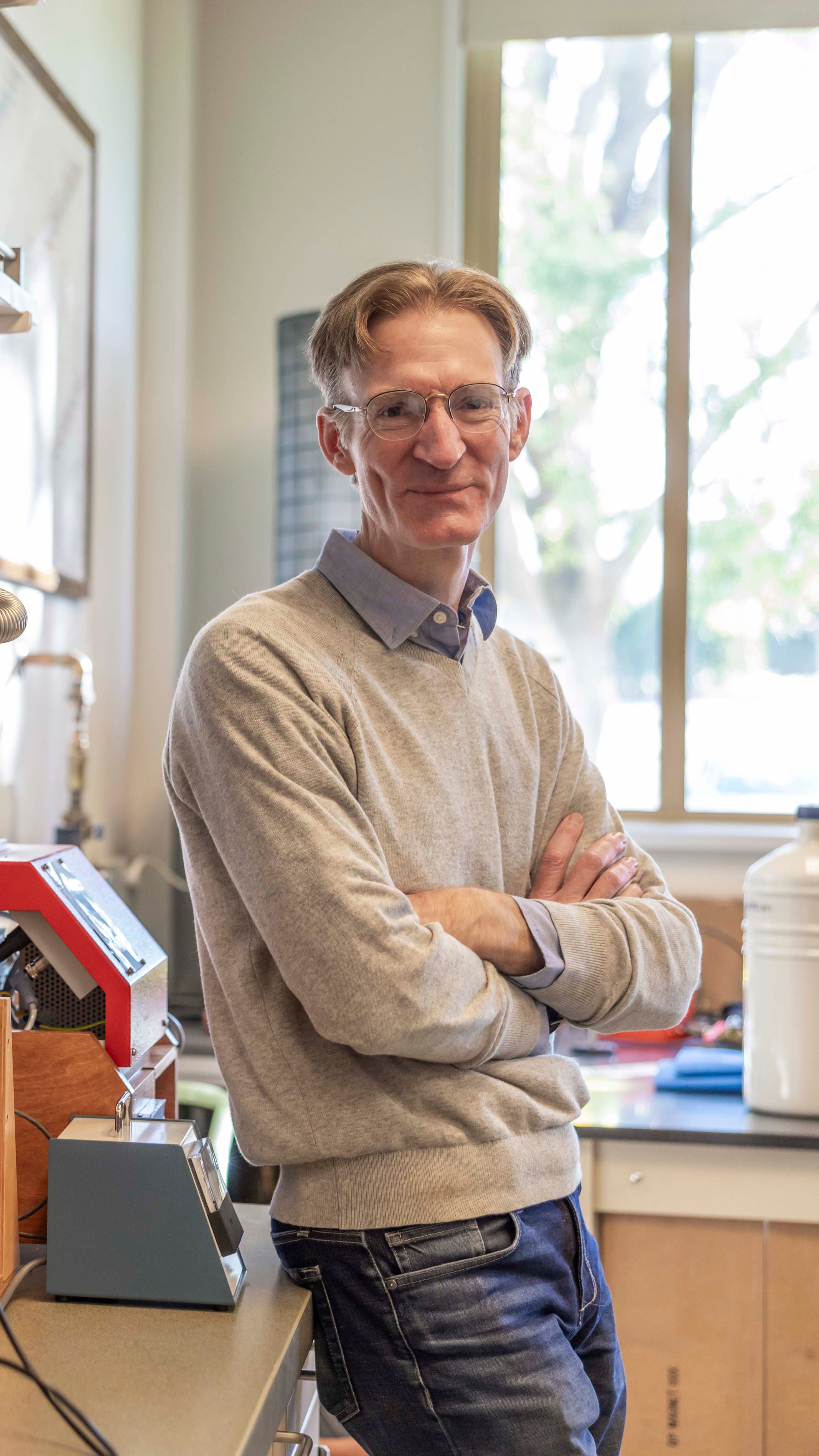 a man with glasses and a sweater with his arms crossed