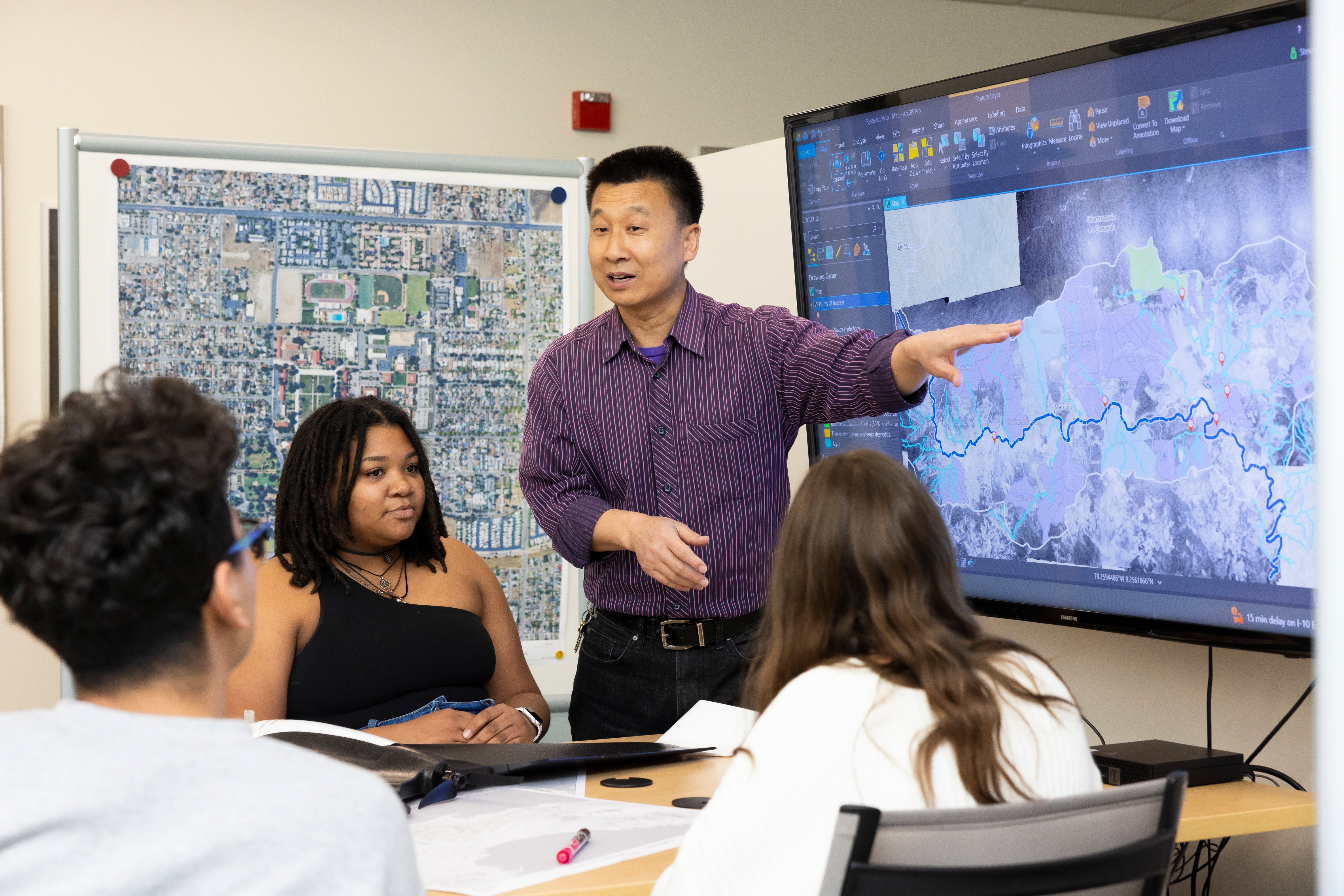 Instructor pointing at map on TV screen with students watching.