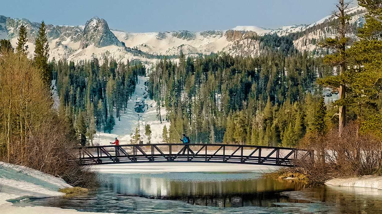 a bridge over a lake with snow covered mountains in the background