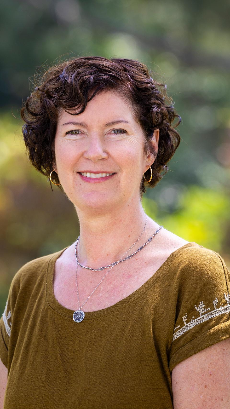 a woman with short curly hair wearing a green shirt and gold earrings