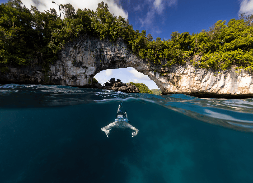 a person swimming under a rock arch