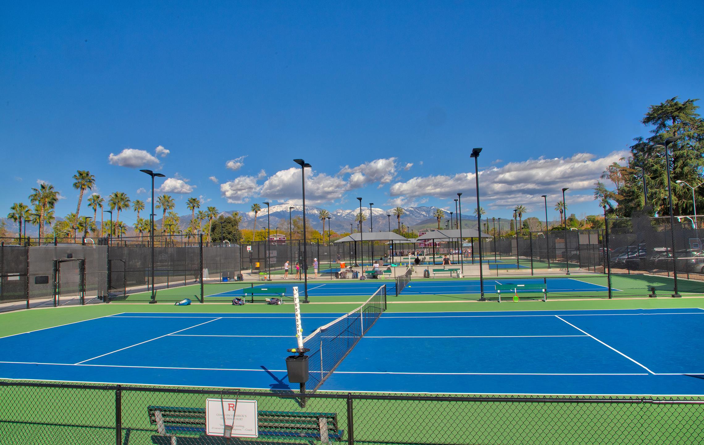 a tennis court with many lights and trees in the background