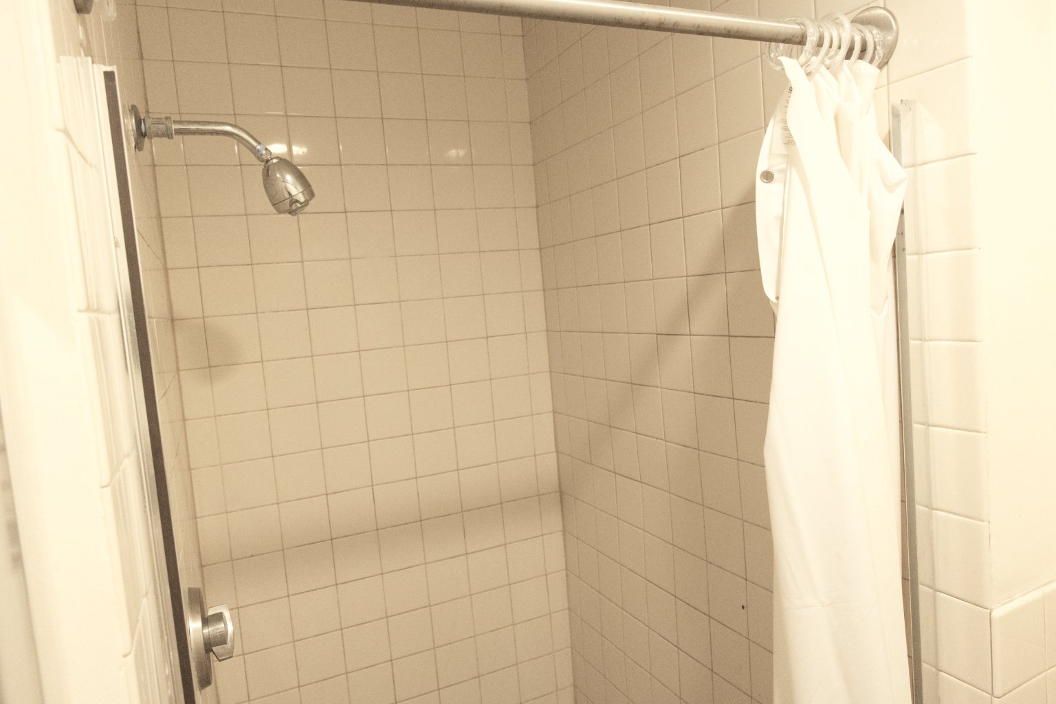 a shower with a shower head and a white shower curtain