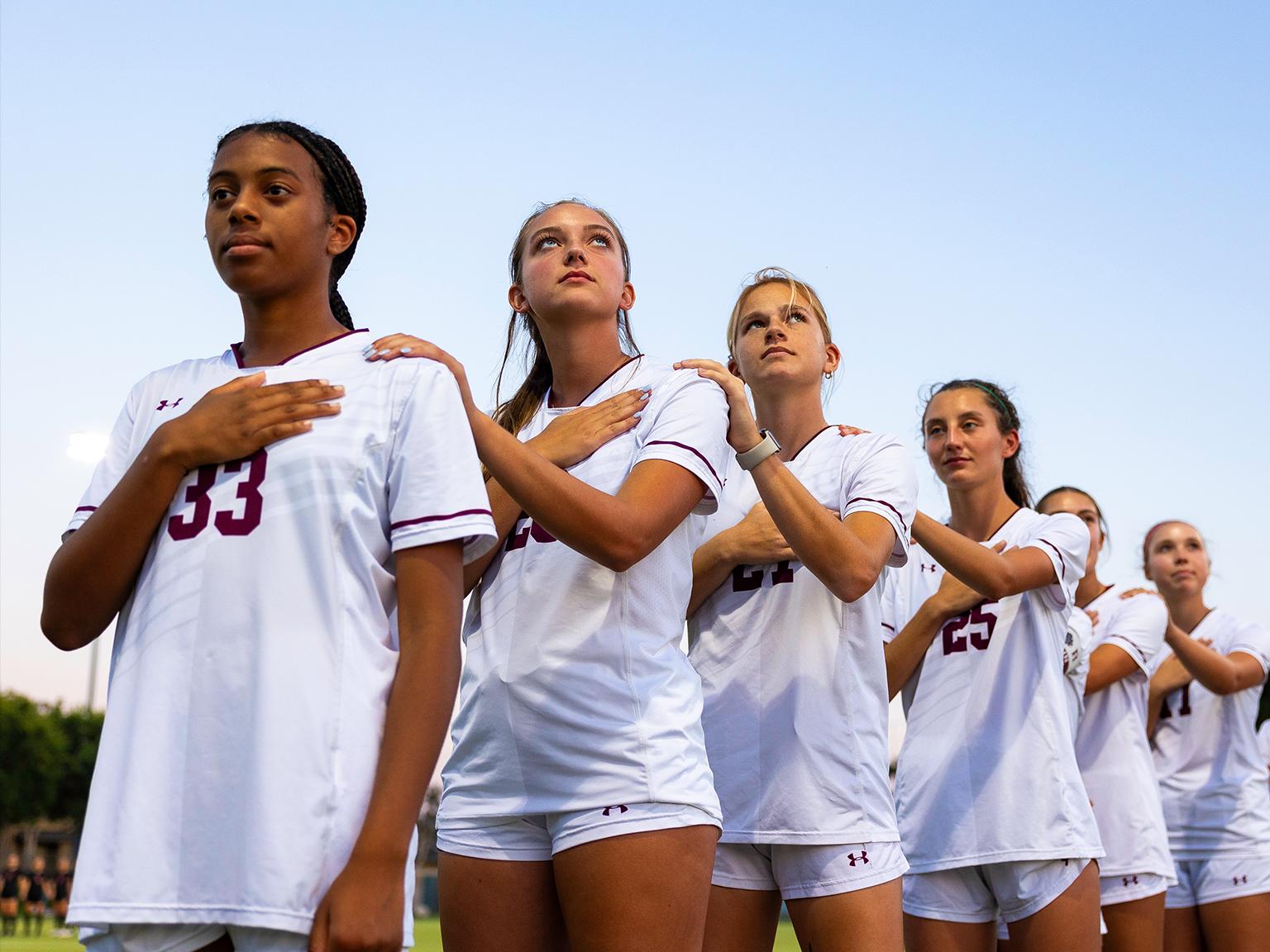 a group of women in white uniforms standing in a line with their hands on their chest