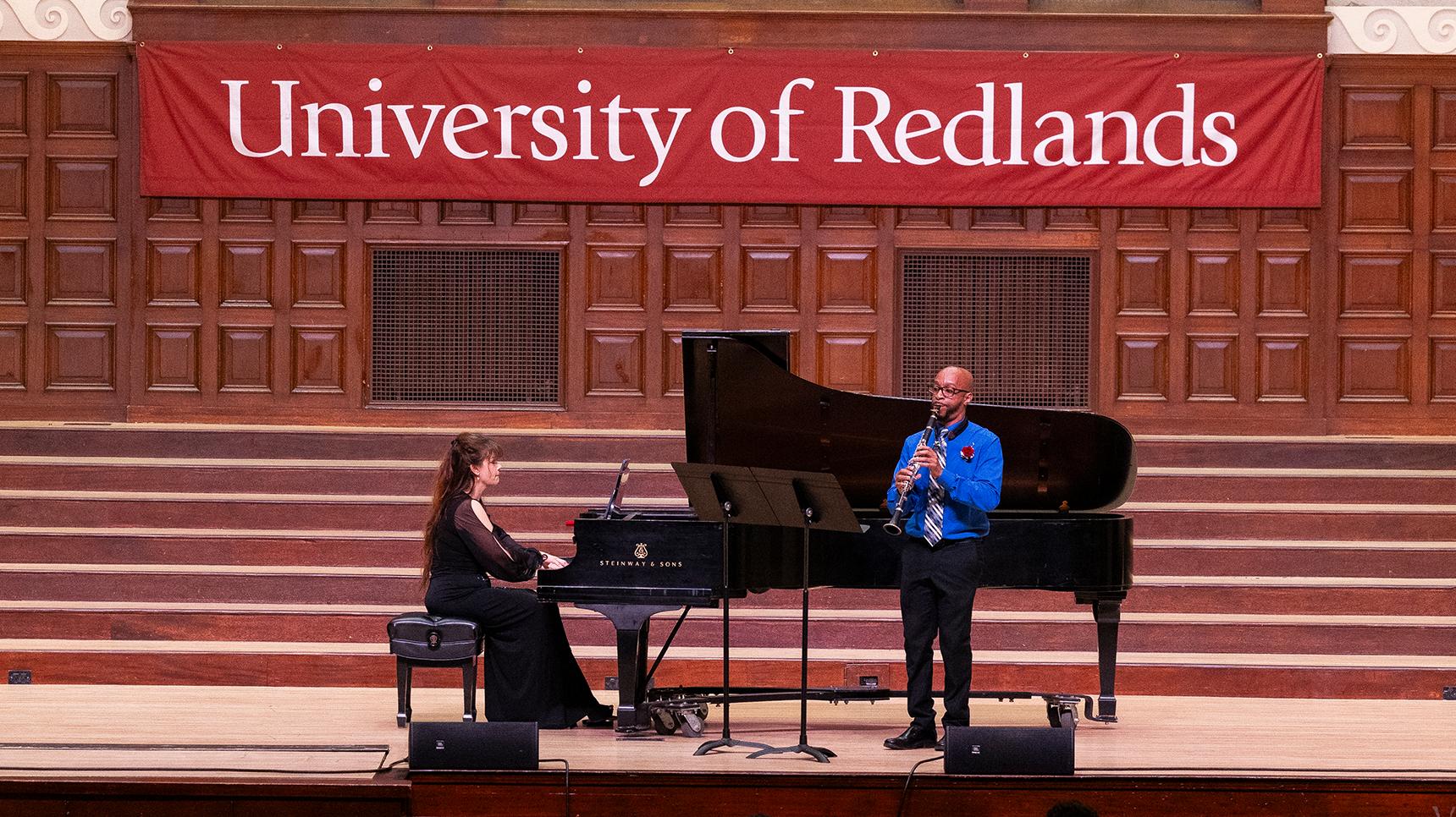 a man playing a flute on a stage with a woman sitting on a piano
