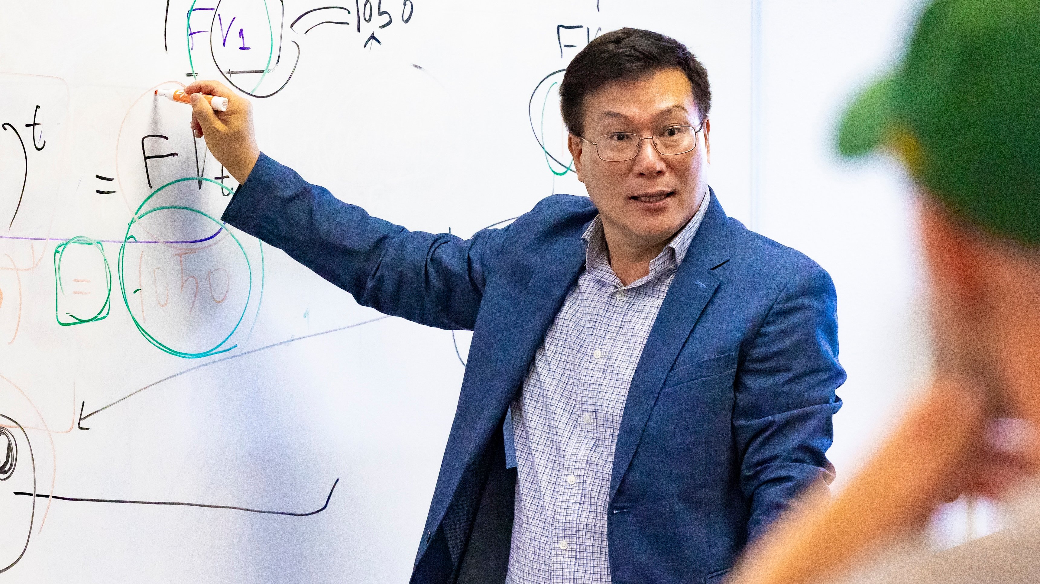 a man in a suit pointing at a whiteboard