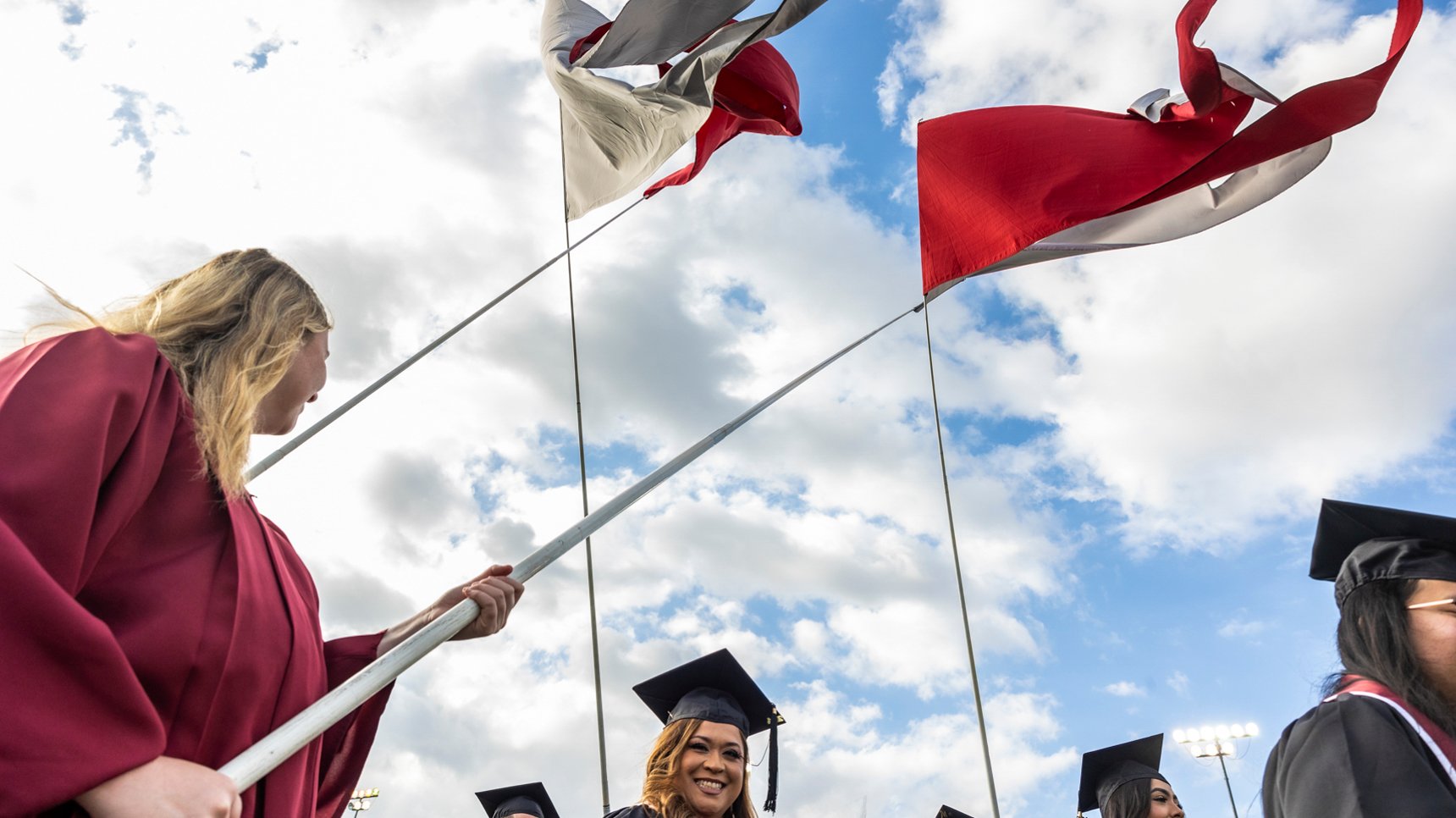 a group of people in graduation gowns and caps holding flags