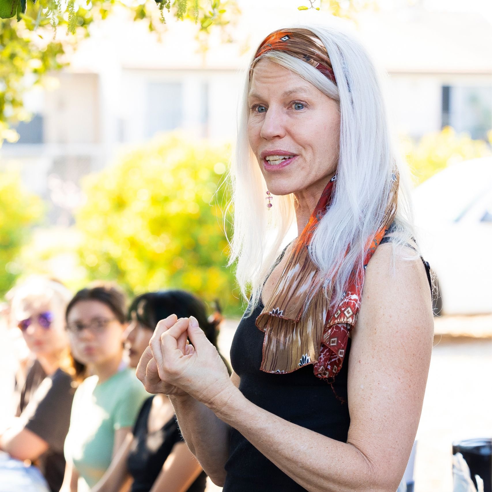 a woman with white hair and a scarf standing in front of a group of people