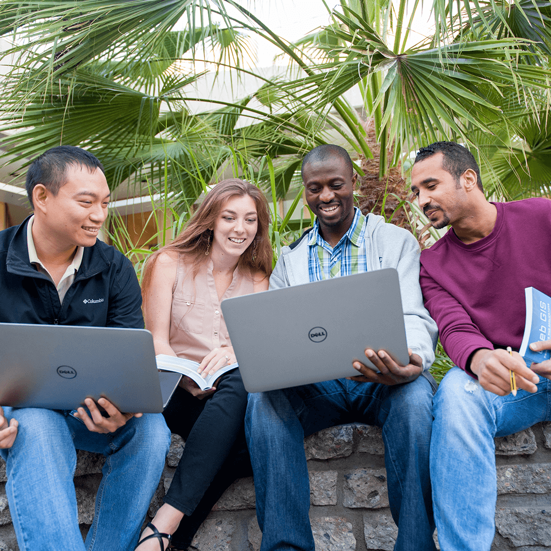 a group of people sitting on a stone wall with laptops
