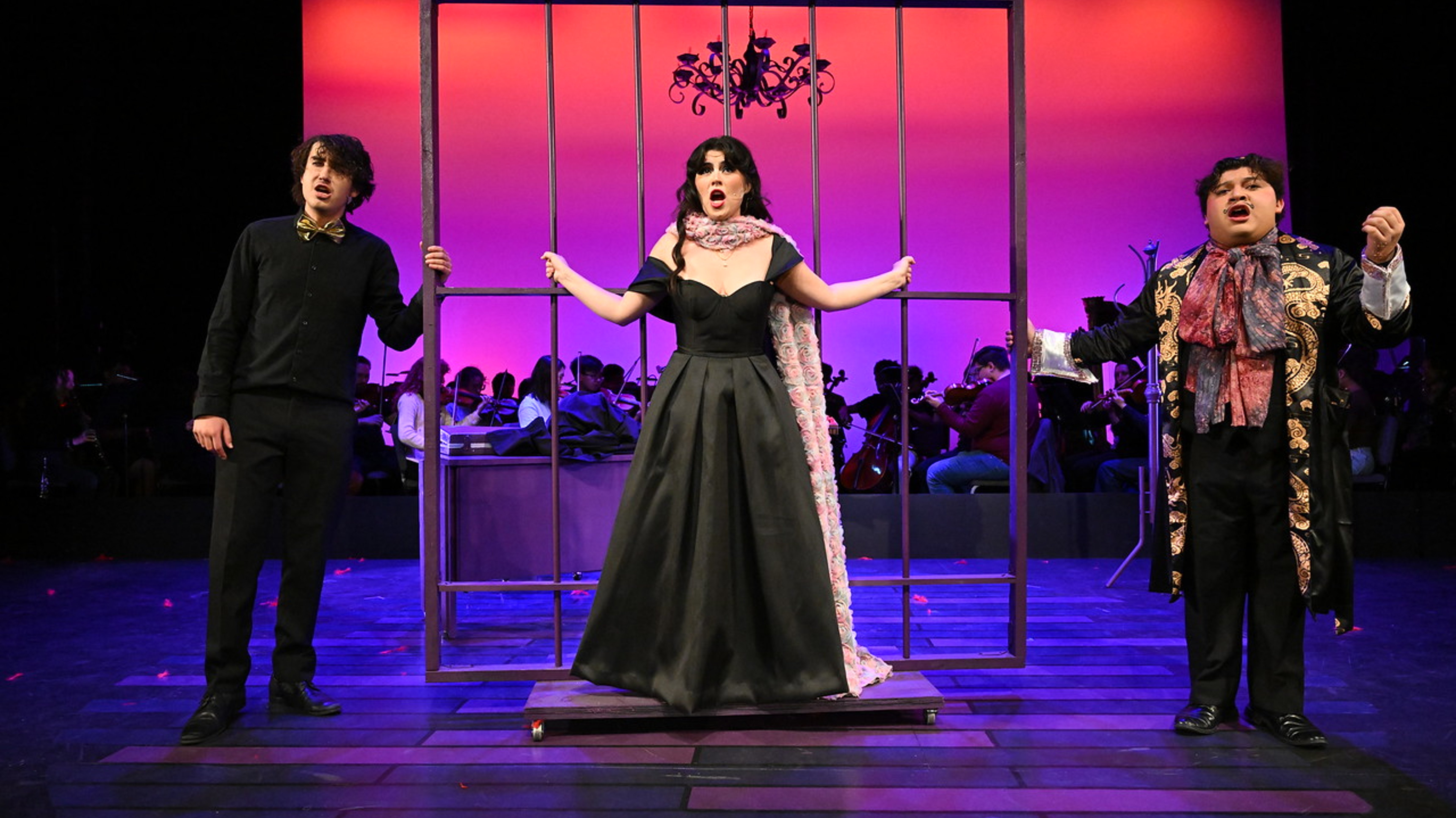 a woman in a black dress standing in front of a cage with a group of people behind her