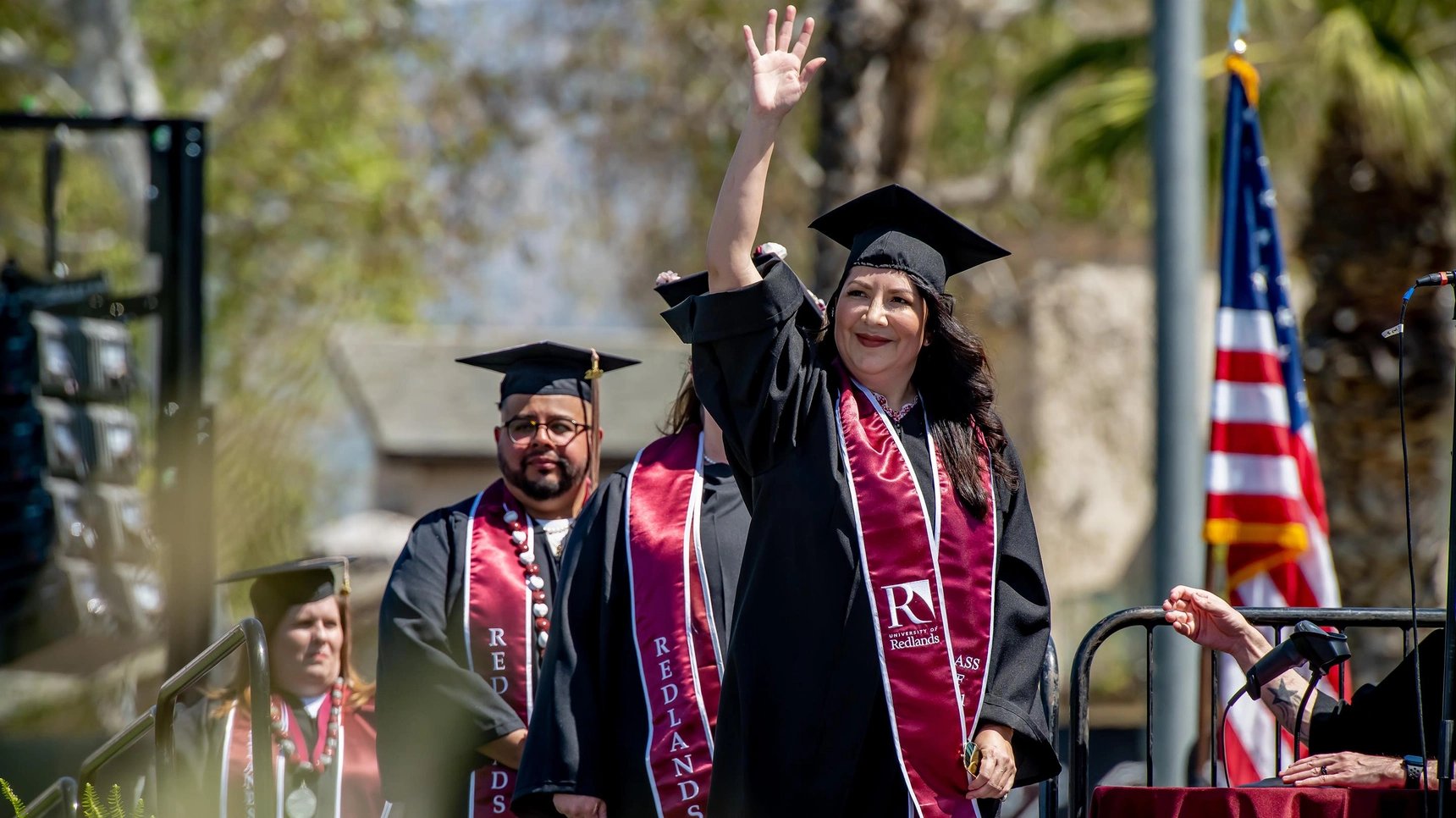 a woman in graduation gown waving