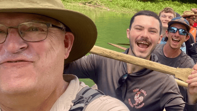 a man in a hat and glasses with a stick in front of a man in a boat