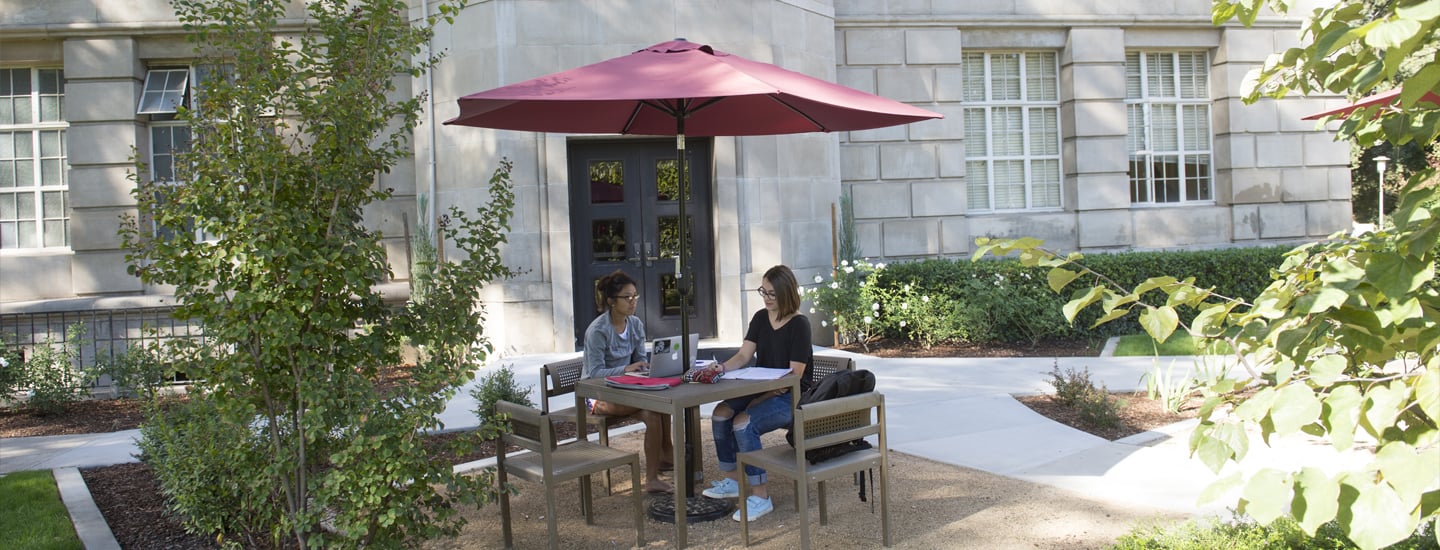 two women sitting at a table under an umbrella