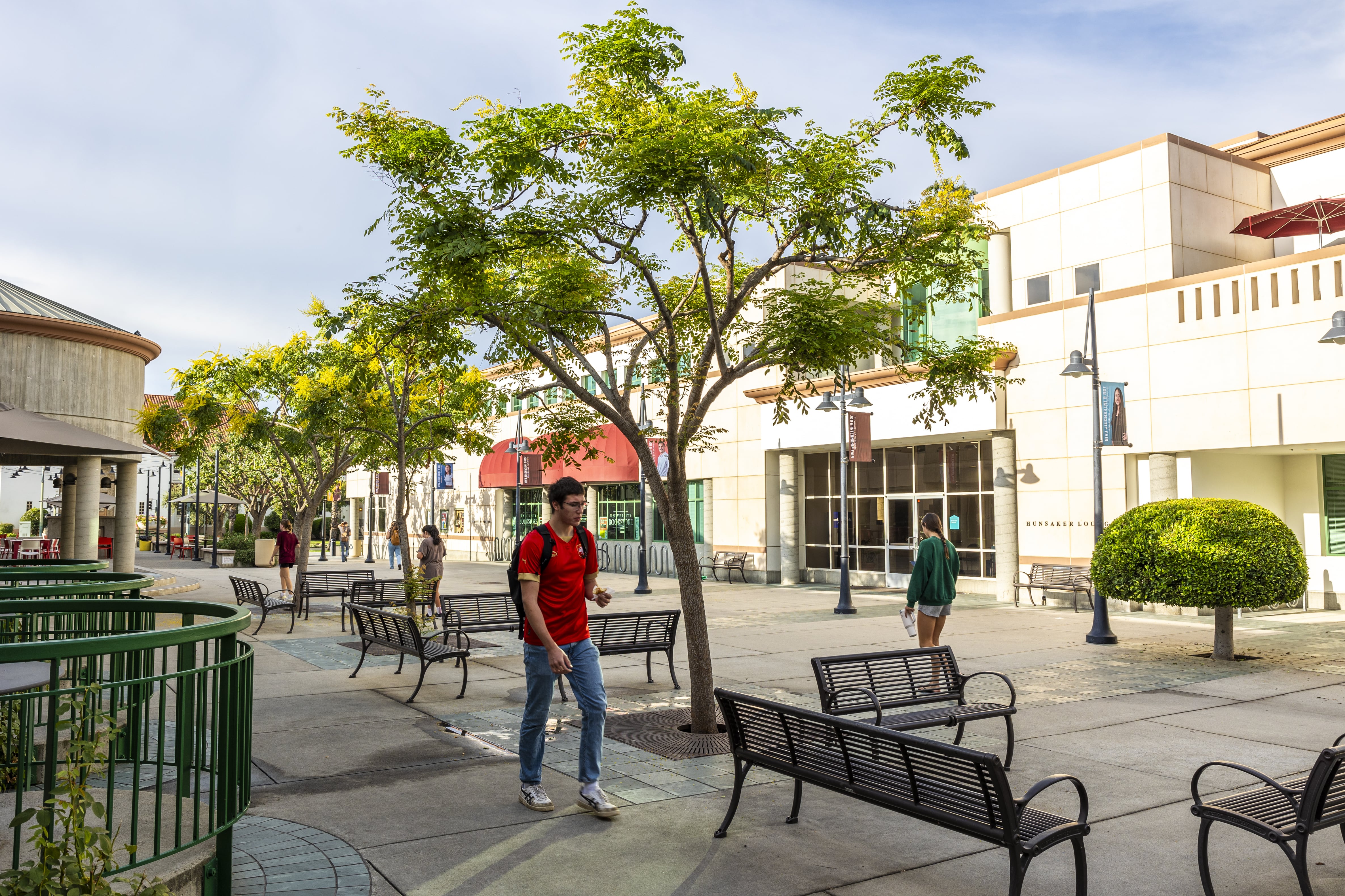 a man walking on a sidewalk with benches and trees