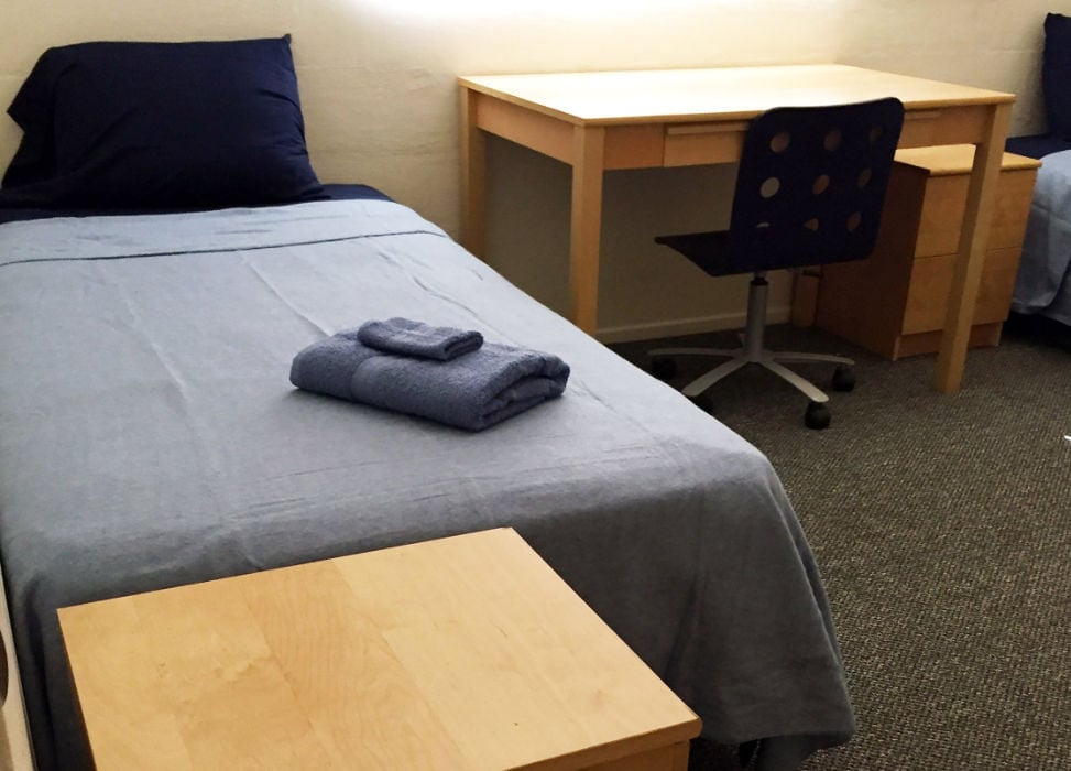 a bed with a blue blanket and a desk