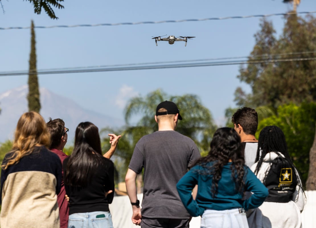 a group of people watching a drone flying over a power line
