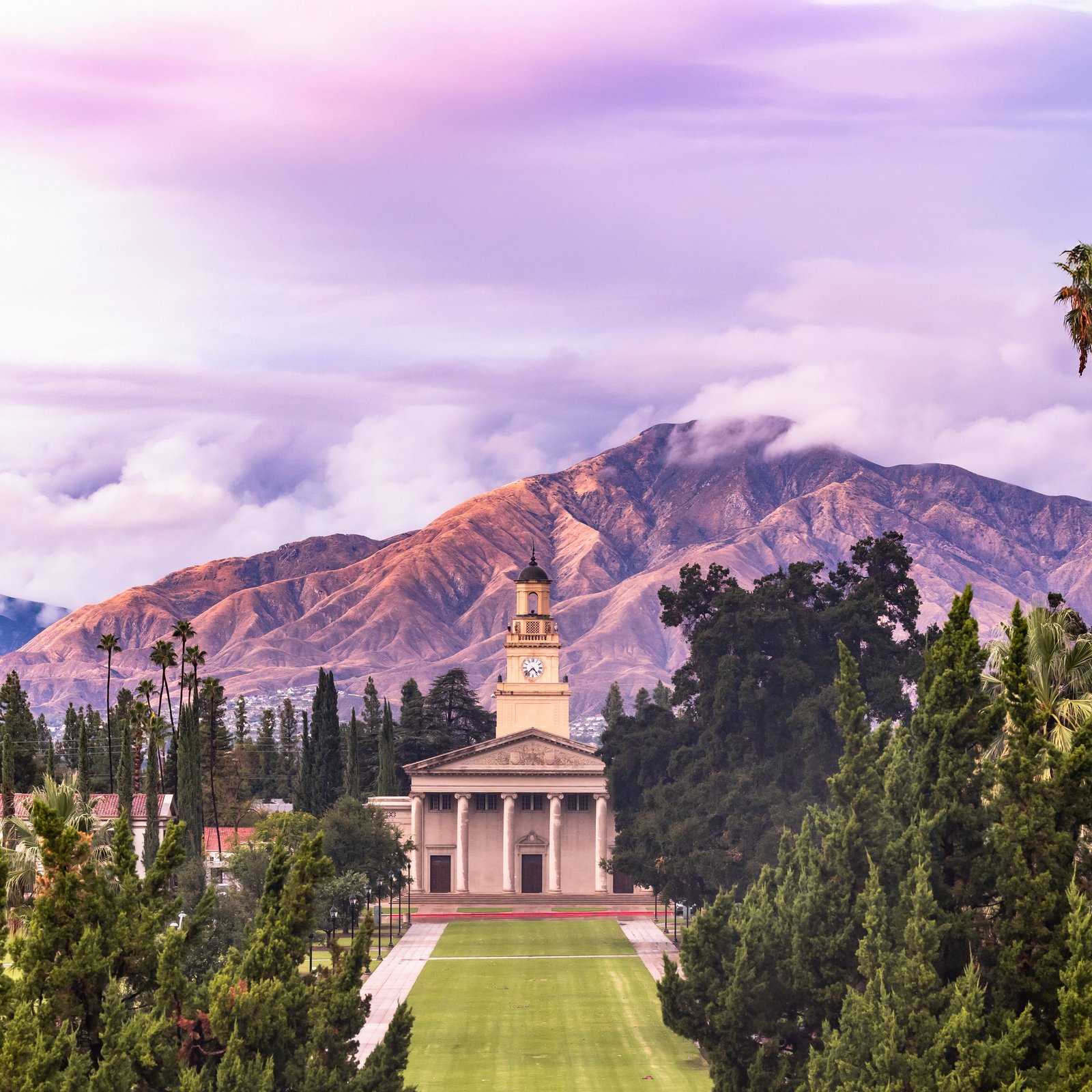 a building with a clock tower and trees and mountains in the background