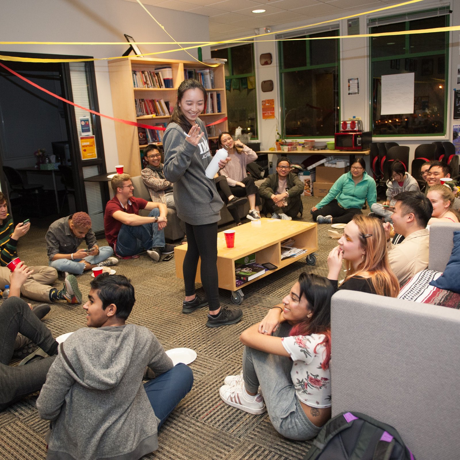 a woman standing in a room with a group of people sitting on the floor