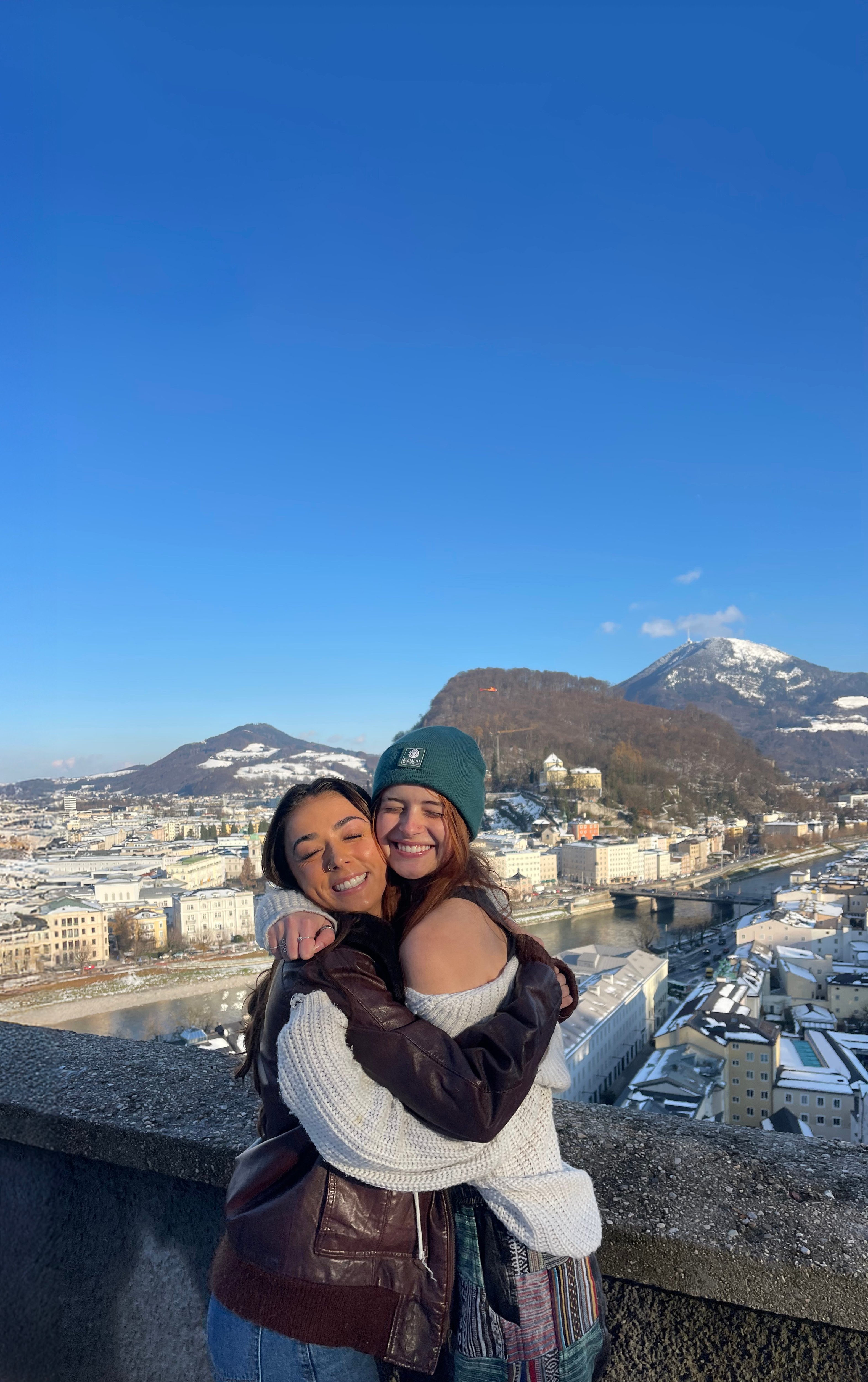 two women hugging each other on a ledge with a city in the background