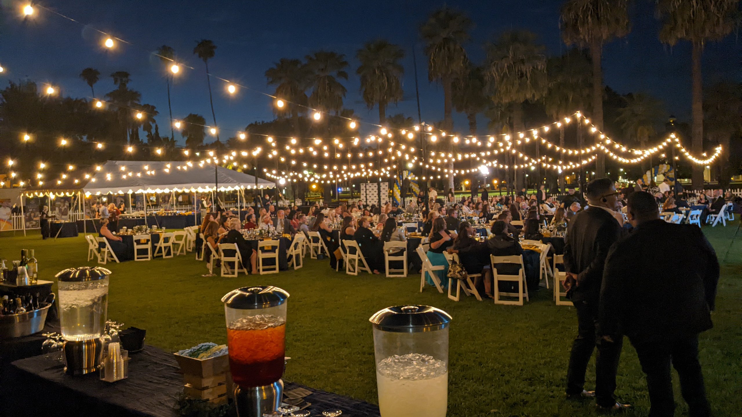 a group of people sitting at tables in a field with lights