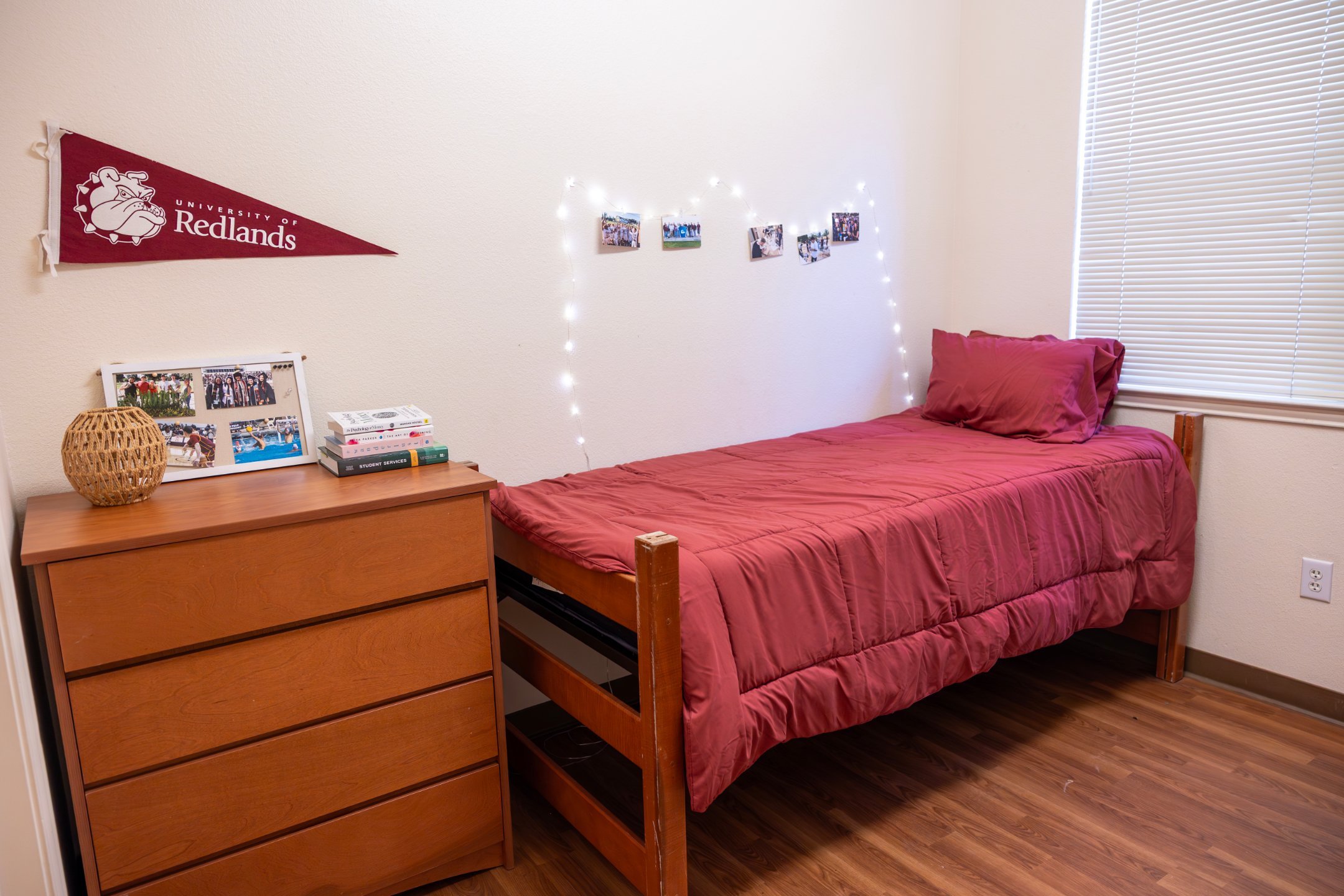 a bed with a red cover and a dresser with lights on the wall