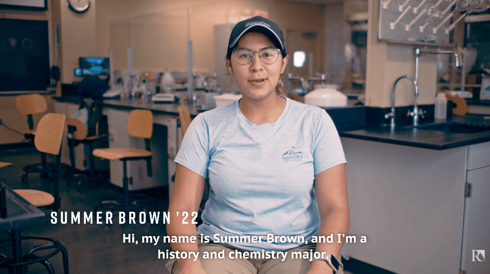 a woman in a blue cap and glasses sitting in a room with a science lab