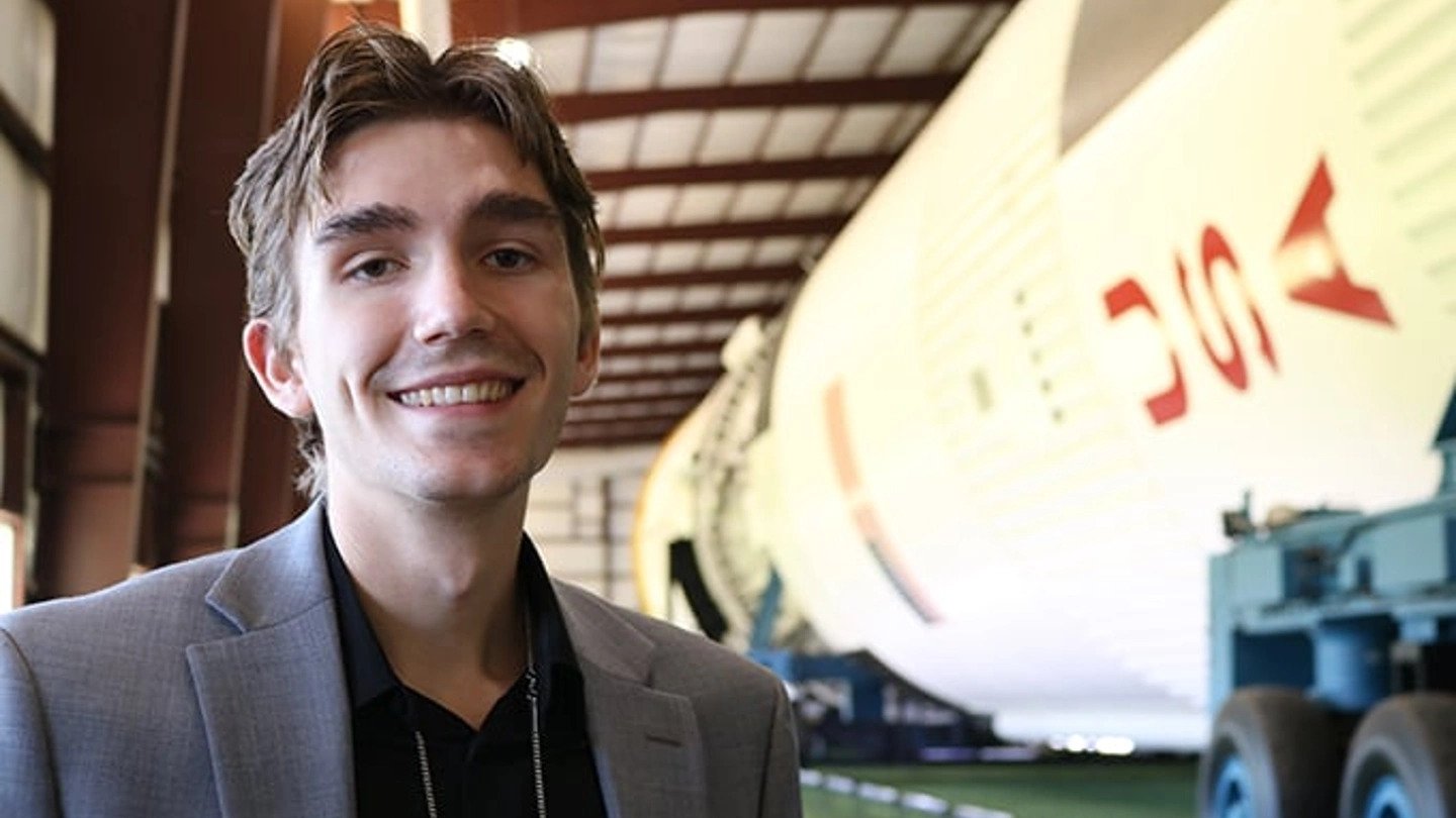 a man smiling in front of a white rocket