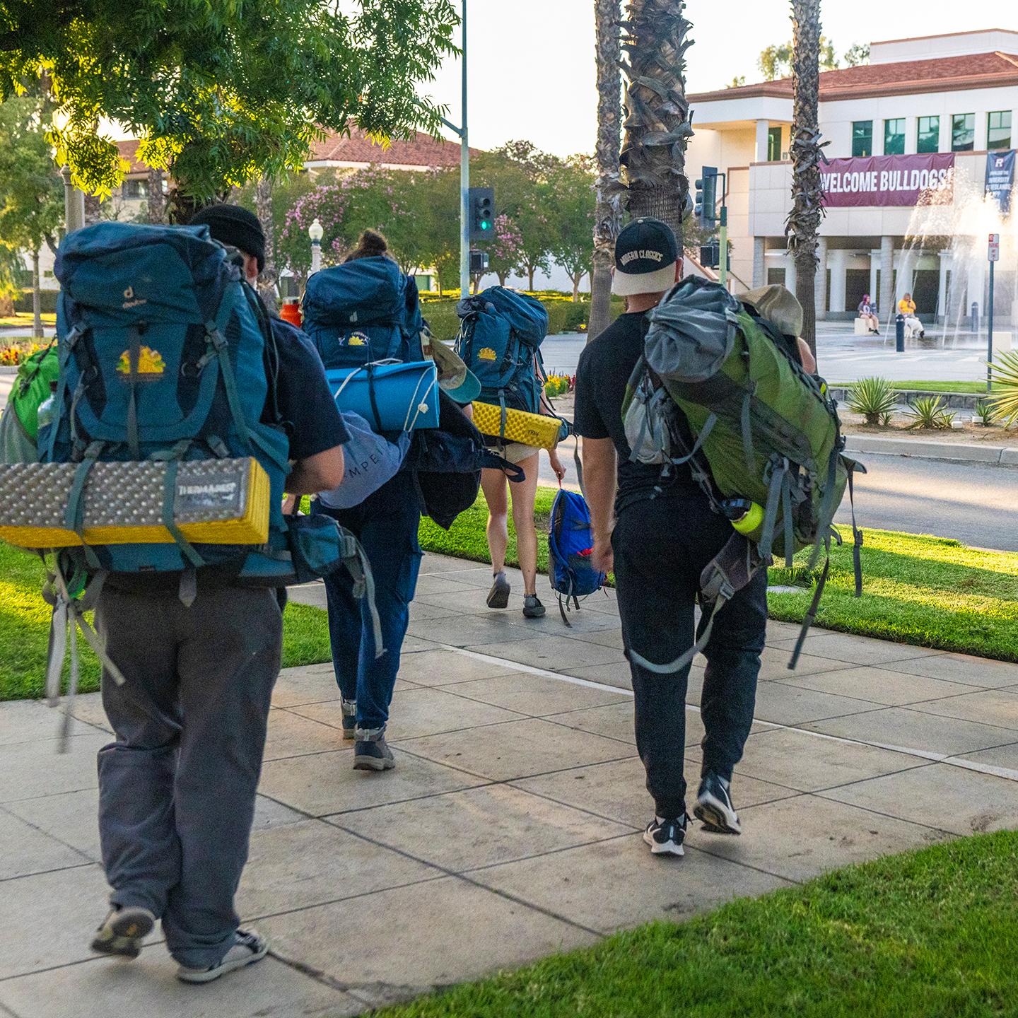 a group of people with backpacks walking on a sidewalk