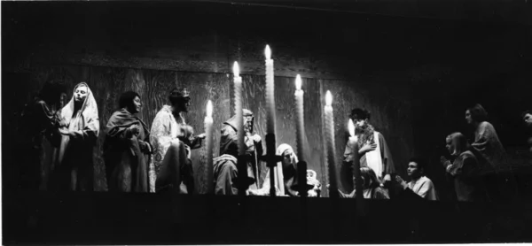 Actors perform a Christmas scene in front of candlelight