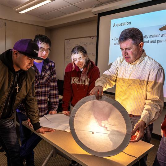 GIS professor teaching students using light and maps.