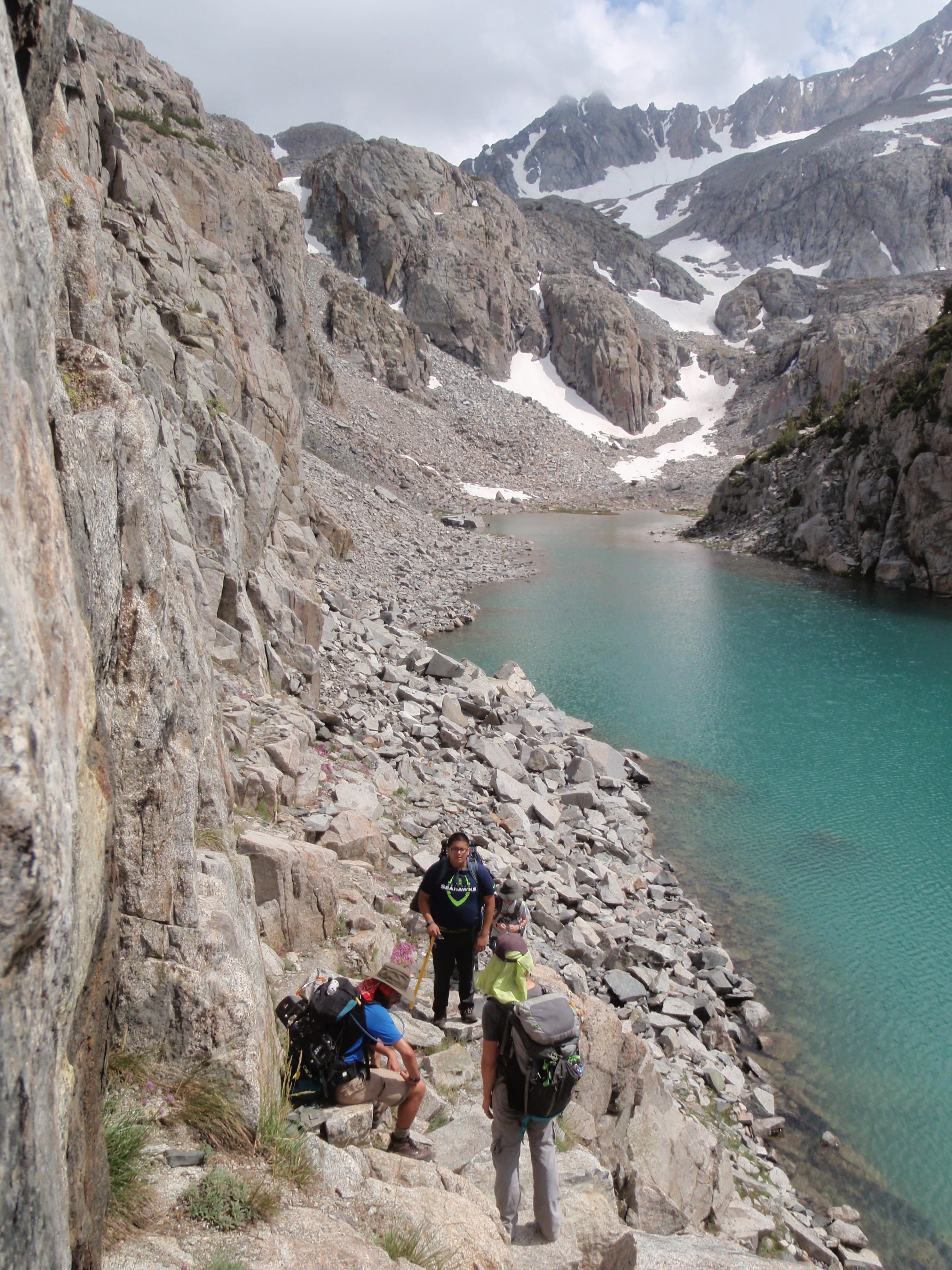 a group of people hiking on a rocky trail by a body of water